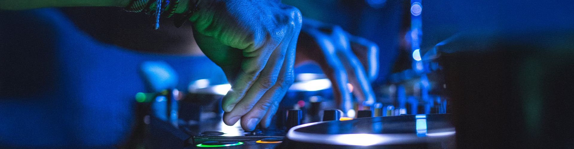 Nahaufnahme von Händen an einem DJ-Pult in blauem Licht, im Vordergrund ein Plattenteller.