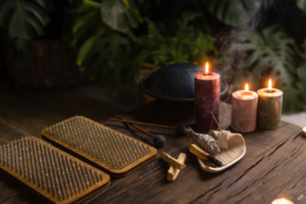 Zwei Holzbretter mit vielen Metallspitzen auf einem Holztisch, daneben brennende Kerzen, eine Handpan, Räucherwerk und Pflanzen