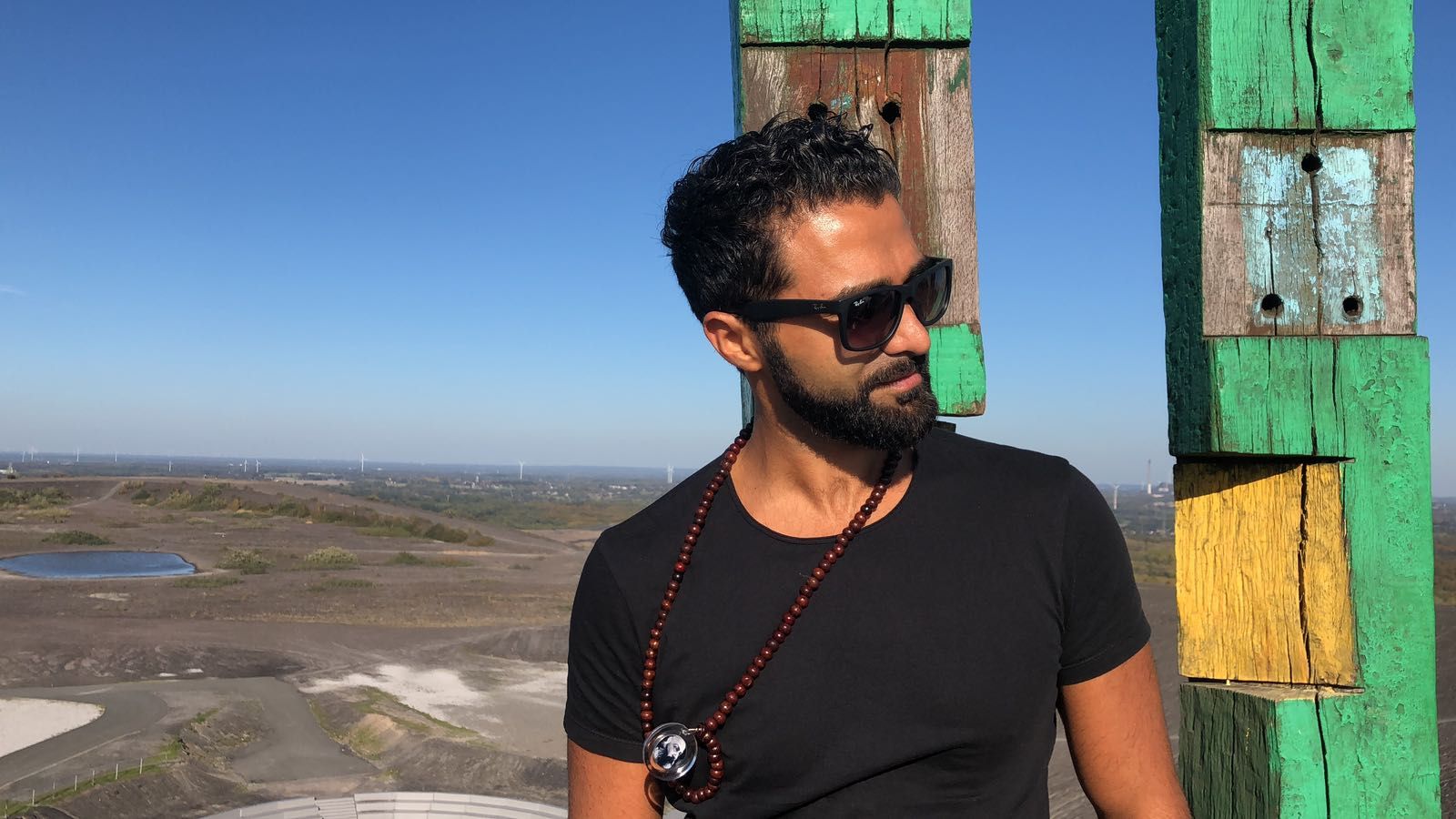 Sohrab Papahn mit Sonnenbrille und Holzperlenkette steht auf einer Anhöhe vor weitem Blick über eine Landschaft