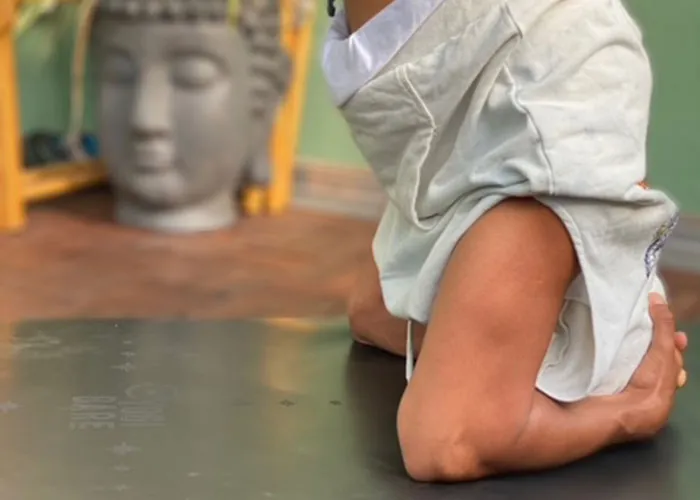 Nahaufnahme einer Person in einer Yoga-Haltung auf einer Matte, im Hintergrund ein Buddha-Kopf aus Stein