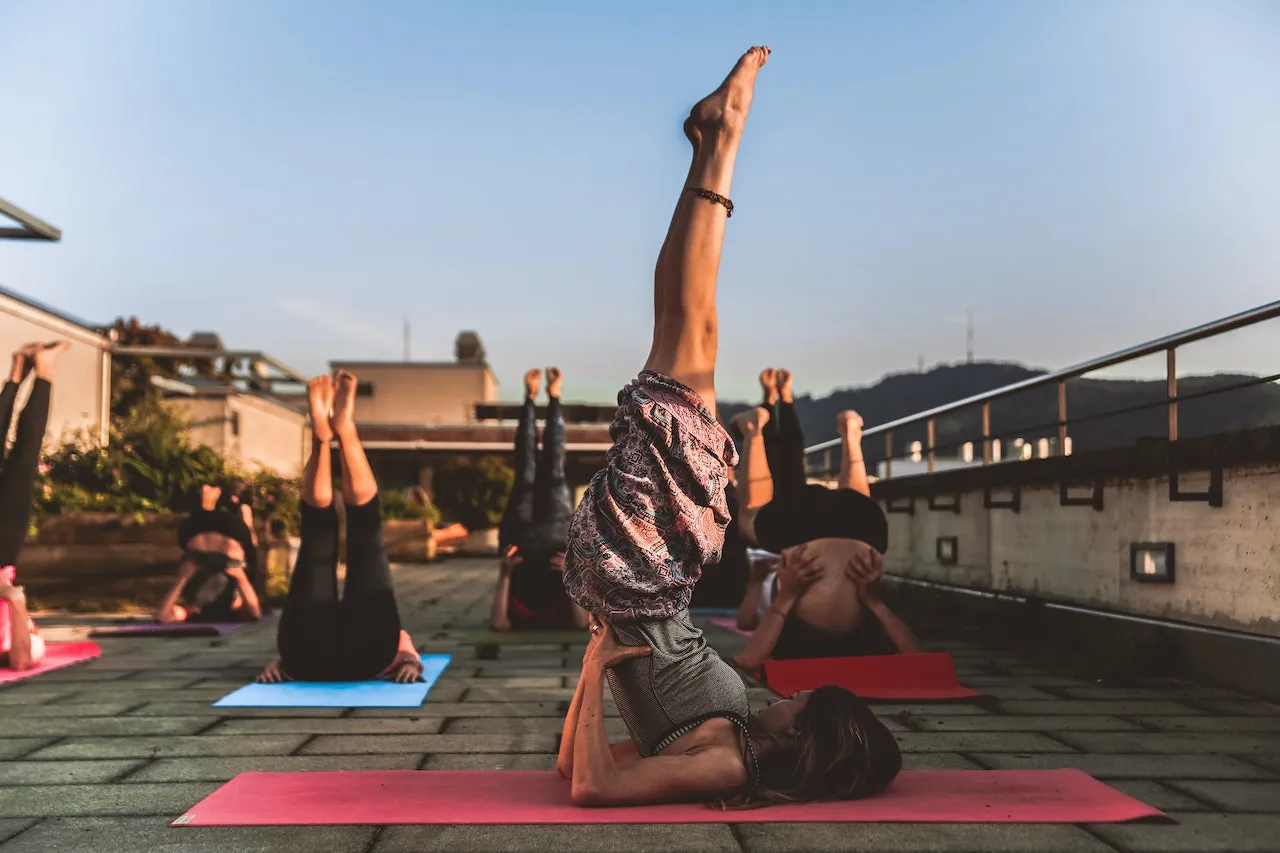 A rooftop yoga class at sunrise, several people in a shoulder stand on colourful mats