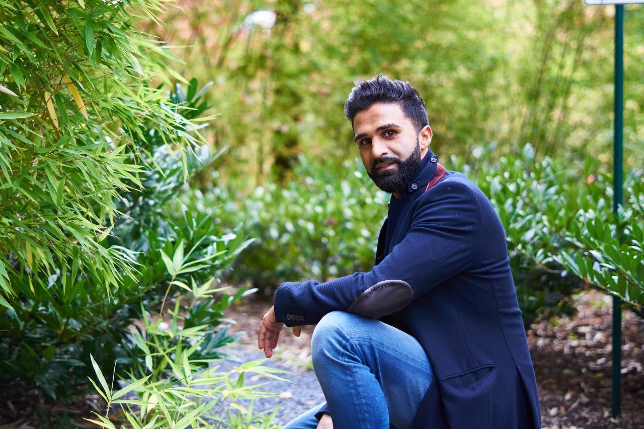 Sohrab Papahn in dunkelblauem Sakko und Jeans hockt in einem Garten zwischen Bambus und Büschen