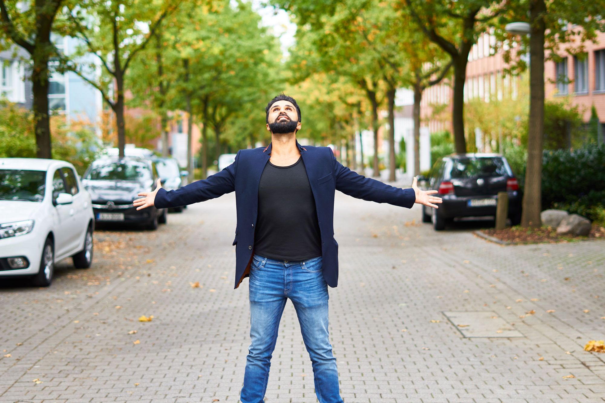 Sohrab Papahn steht mit weit ausgebreiteten Armen auf einer von Bäumen gesäumten Straße und blickt nach oben